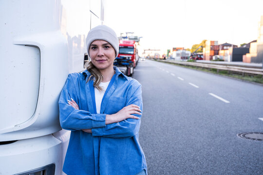 Confident woman truck driver leaning on truck outdoors