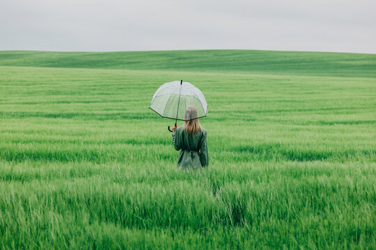 Businesswoman standing in a green wheat field with a transparent umbrella