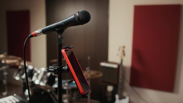 Microphone and smartphone on stand standing in music recording studio with drums in background. Footage is suitable for promos about mobile recording apps, online music lessons, or podcasting
