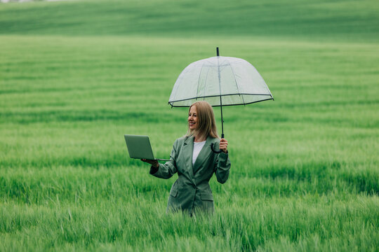 Businesswoman works on laptop under an umbrella in green field