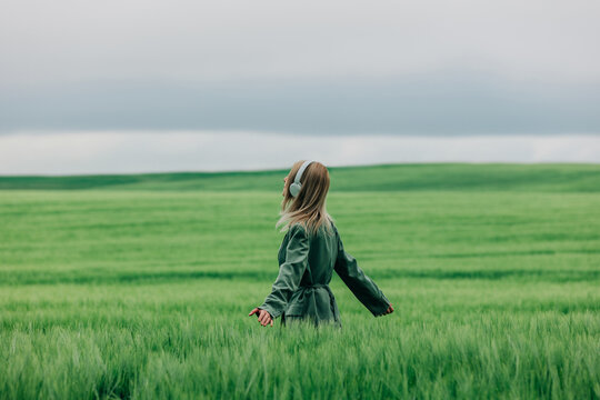 Female manager in green suit listening to music in wheat field