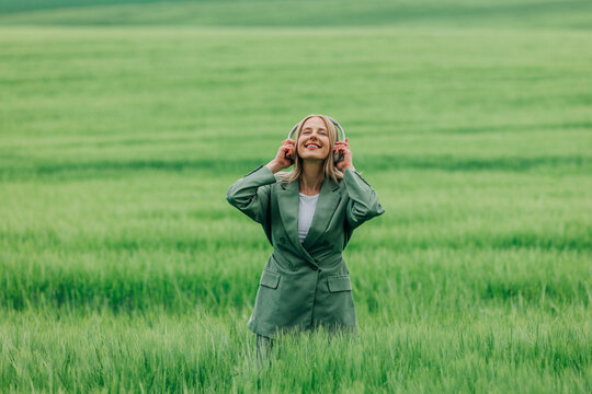 Businesswoman enjoying music and freedom in a green spring wheat field