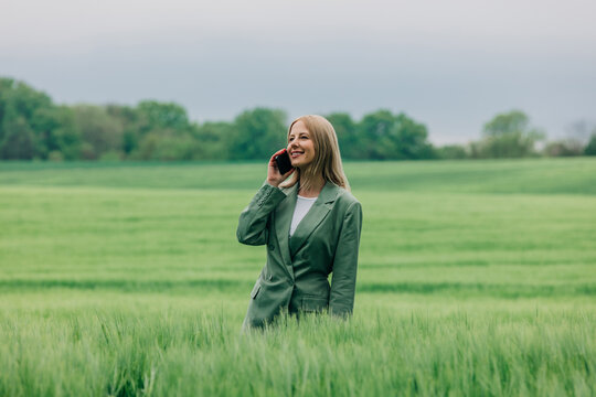 Smiling businesswoman talking on smartphone in green wheat field