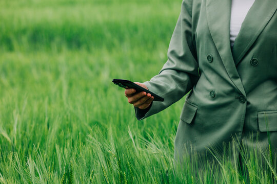 Businesswoman in green business suit holding smartphone in wheat field