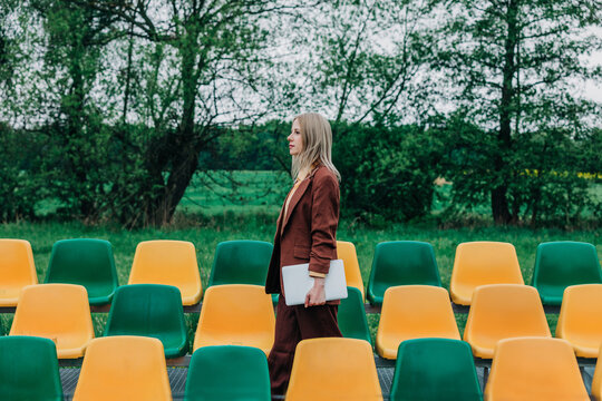 Freelancer walking past colorful chairs outdoors with laptop