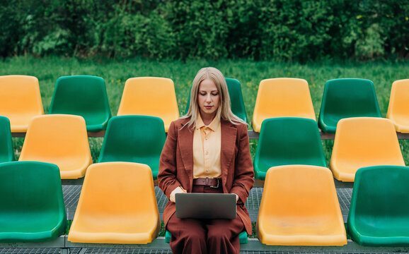 Businesswoman working on laptop on empty outdoor stadium seats
