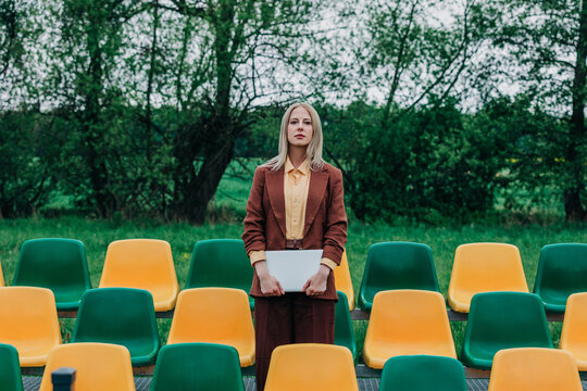 Businesswoman holding laptop by empty stadium seats outdoors