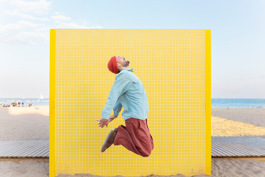 Energetic tourist jumping in superhero pose on a sunny beach