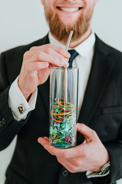 Smiling businessman holding glass of stationery with a straw