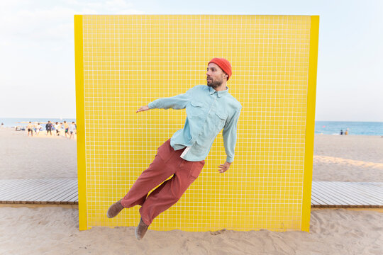Energetic superhero jumping by a yellow tiled wall on the beach
