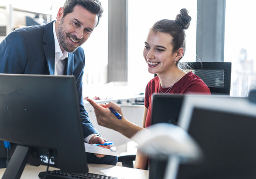 Manager and employee smiling and pointing at computer in office