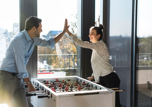 Colleagues giving high five playing tablesoccer in the office