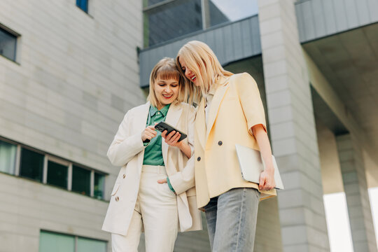 Businesswomen look at a smartphone outside a modern office