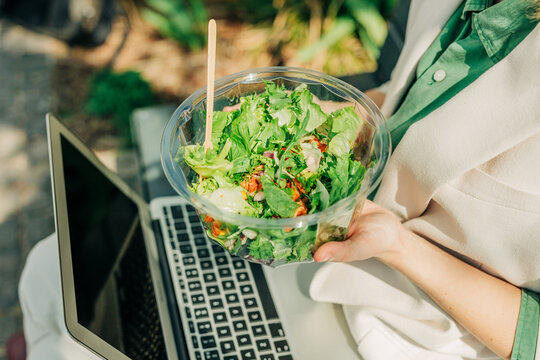 Eating a healthy salad lunch outdoors while working on a laptop