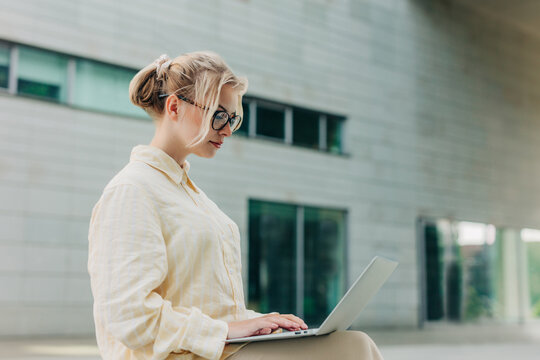 Applicant typing on laptop outdoors near modern architecture