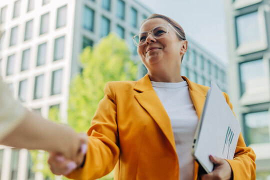 Smiling businesswoman shaking hands outdoors during a corporate meeting
