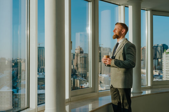 Smiling businessman relaxing with coffee by window in sunny office