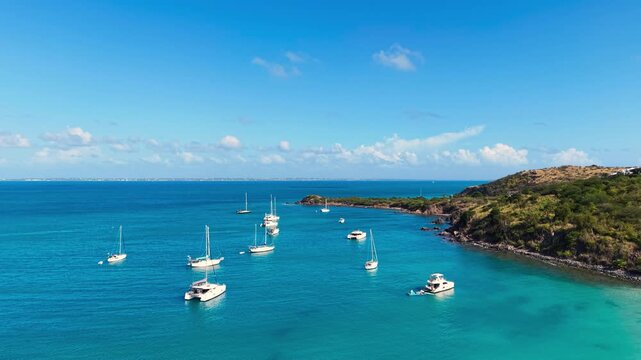 Drone view of sailboats and catamarans anchored in a calm tropical bay near Friar's Bay Beach on Saint Martin island. The turquoise ocean waters surround the lush green coastline Caribbean destination