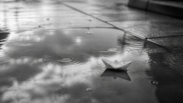 Paper Boat Floating In Rain Puddle On Pavement