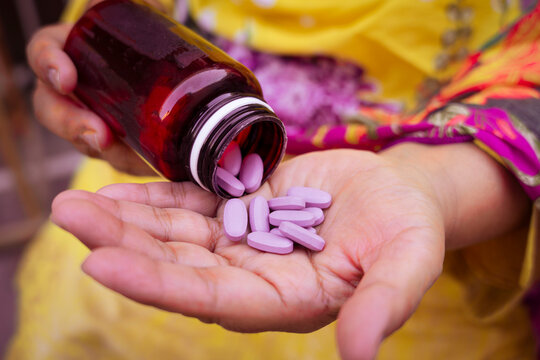 Hand holding open amber bottle dispensing purple oval tablets with medication pharmacy healthcare medicine prescription pharmacology supplement treatment pharmaceutical wellness recovery