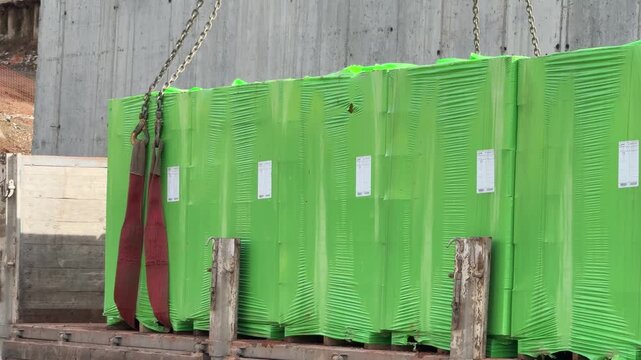 Green wrapped aerated concrete blocks being lifted from a truck bed with crane chains and slings on site [cite: AAA_3.jpg]. Construction materials logistics and supply chain