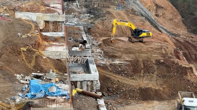 Yellow crawler excavator performing slope excavation and ground leveling on a steep site [cite: HH.jpg]. Geotechnical project, foundation and concrete retaining wall construction