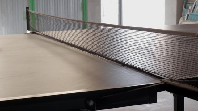 Orange ping pong ball bounces on table tennis table in bright indoor setting
