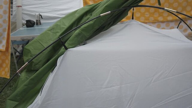 Rainfly being placed over tent frame at outdoor campsite with table nearby