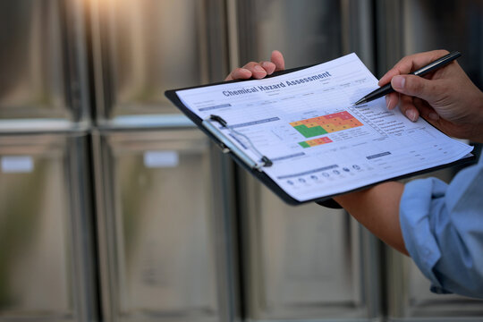 Serious inspector holding chemical hazard assessment form with diligent concentration in professional industrial facility outdoor