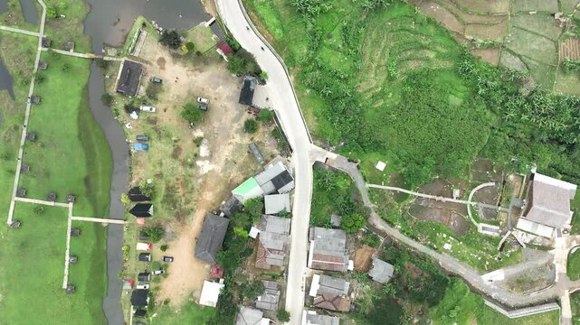 Aerial view of Rawa Gede Jonggol Lake area with rural houses, a winding road, and lush green fields in Kecamatan Sukamakmur, Jawa Barat, Indonesia.
