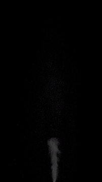 Hot Steam Plume. Slow-motion of hot steam powerfully rising from below, forming a tall turbulent column that expands, gradually dissipates into fine sparkling particles against deep black background.