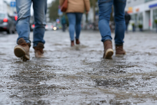Wet pavement reflects city's damp, rainy atmosphere. People walk away, boots sinking slightly into puddles. Their pace suggests routine, indifferent to weather's chill. Urban setting feels ordinary
