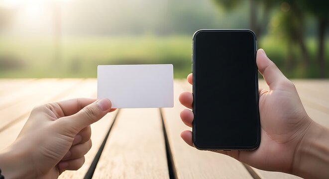 Hands holding a blank card and smartphone outdoors on wooden table