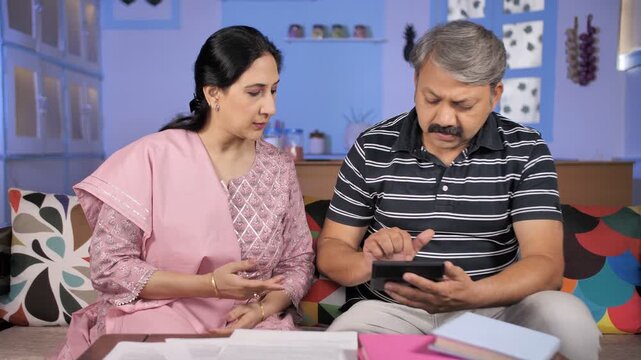 Worried retired couple doing paperwork and discussing their unpaid bills / taxes. Elderly Indian husband-wife stressed while checking their bank statements on mobile and papers - financial problems