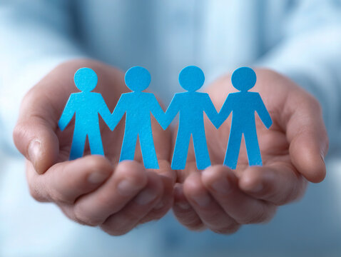 Person holding blue paper cutout figures of people standing hand in hand symbolizing teamwork unity and community support in a cooperative environment