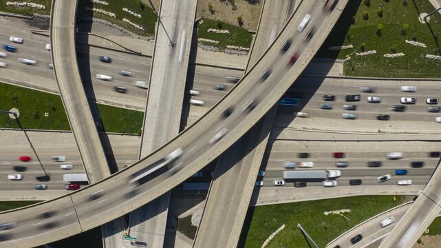 Top down elevated time lapse capturing intense traffic flow on interchange, multi level complex freeway infrastructure with cars commuting on ramps