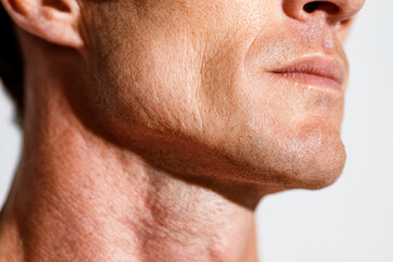 Fototapeta premium Profile view of a mature man?s lower face and neck showing natural skin texture and subtle facial hair against a plain light background