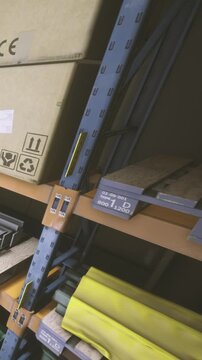 Shelves in a warehouse display a yellow object on wooden pallets. The setting is simple with brown wood and dim lighting. The focus is on organization within the space.