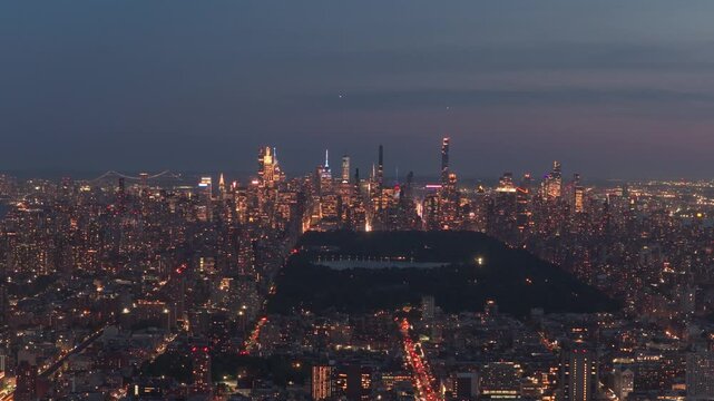 Nighttime panorama of Manhattan skyline showing Central Park, Midtown skyscrapers, surrounding districts of South Bronx with glowing city lights from high angle