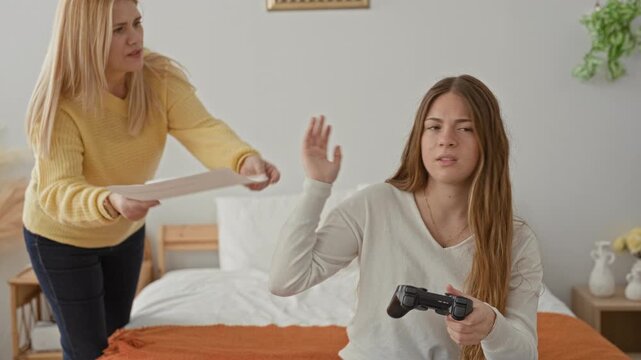 Woman hands paper to daughter while girl grips controller on bed in building; tension family conflict.