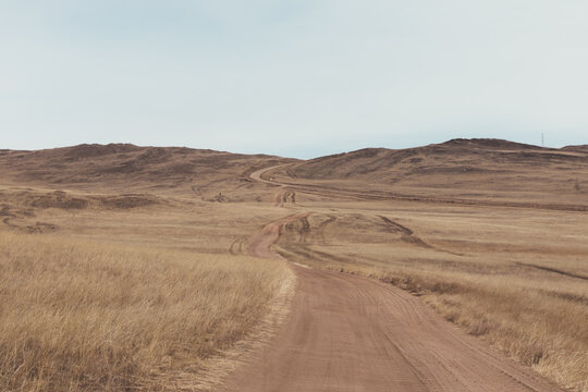 Scenic winding dirt road crossing dry steppe hills on Olkhon Island, Irkutsk Oblast, Russia, near Lake Baikal, with vast open space and cloudy sky