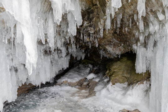 Close-up of large icicles and ice formations hanging from a rocky cave with snow and frozen water on the shore of Lake Baikal, Irkutsk Oblast, Russia