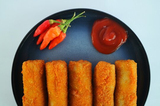 This is risoles (or risol), a popular Indonesian snack with a rough, crispy outer crust and a soft, sliced ​​chicken filling. It's served on a black plate with chili sauce and red chili.