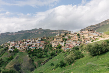 Obraz premium Wide landscape view of Chokh aul, a traditional mountain village built on a steep hillside in Dagestan, Russia, with terraced homes, green slopes and cloudy sky