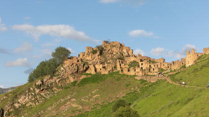 Fototapeta premium Panoramic view of the ruins of Gamsutl, an abandoned stone mountain village on a hillside in the Republic of Dagestan, Russia, under blue sky and clouds