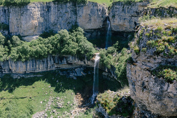 Fototapeta premium Wide landscape view of Matlas waterfalls dropping from high limestone cliffs into a green canyon near Matlas village, Khunzakh District, Dagestan, Russia