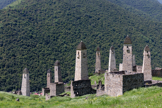 Scenic view of the medieval Erzi tower complex with traditional stone watchtowers and ruins on a grassy hillside, Dzheyrakh District, Ingushetia, Russia