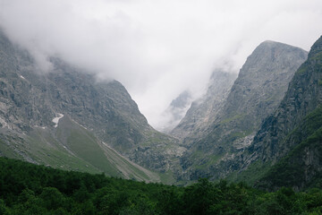 Obraz premium Dramatic view of Midagrabin Waterfalls gorge with steep rocky mountains, low clouds and green forest in North Ossetia–Alania, Russia, Caucasus region