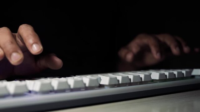 Hands typing on keyboard in dark workspace, Close-up of hands typing on a white computer keyboard in low light with dark background