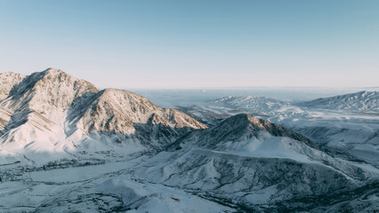 Obraz premium Aerial winter view of snow-covered mountains and valleys in Chunkurchak Valley near Tatyr, Chuy Region, Kyrgyzstan, with clear sky and distant ridgelines